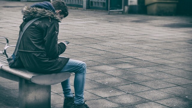 Man sitting on bench wearing skinny jeans and a parka jacket